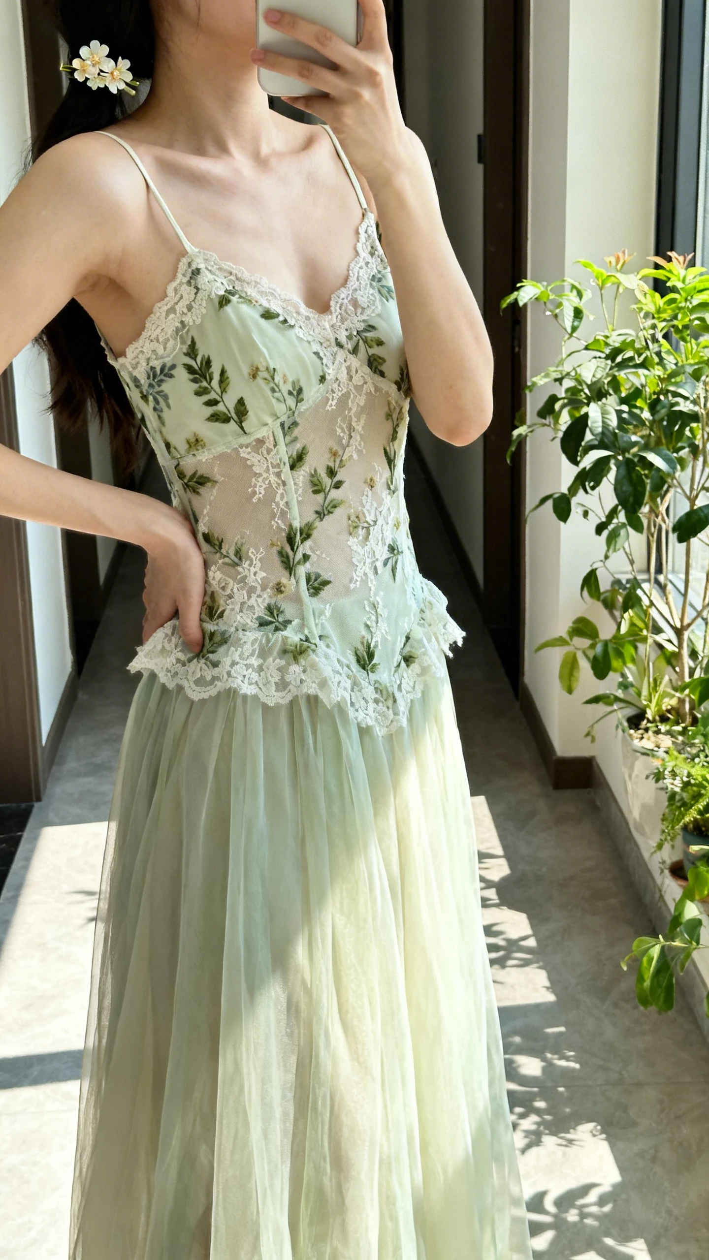 iPhone side-angle selfie of a woman wearing a garden nymph lace slip dress with an airy overskirt, botanical lace details, thin straps, dainty floral hairpin, face not visible, taken in a sunlit hallway near plants, natural morning light, casual iPhone aesthetic