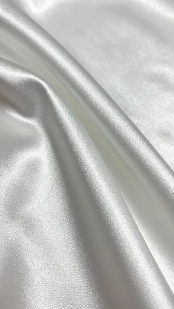 Close-up shot of satin fabric textures: smooth satin and a subtly textured satin swatch held against a light source to show different levels of shine and dimension, no accessories.