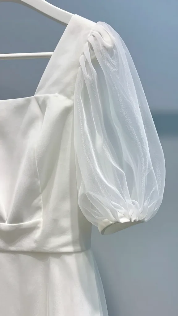 Close-up of a white organza balloon-sleeve gown on a hanger against a pale blue backdrop, intricate sleeve volume, subtle shimmer in the fabric, focus on the texture and breathability of the material.