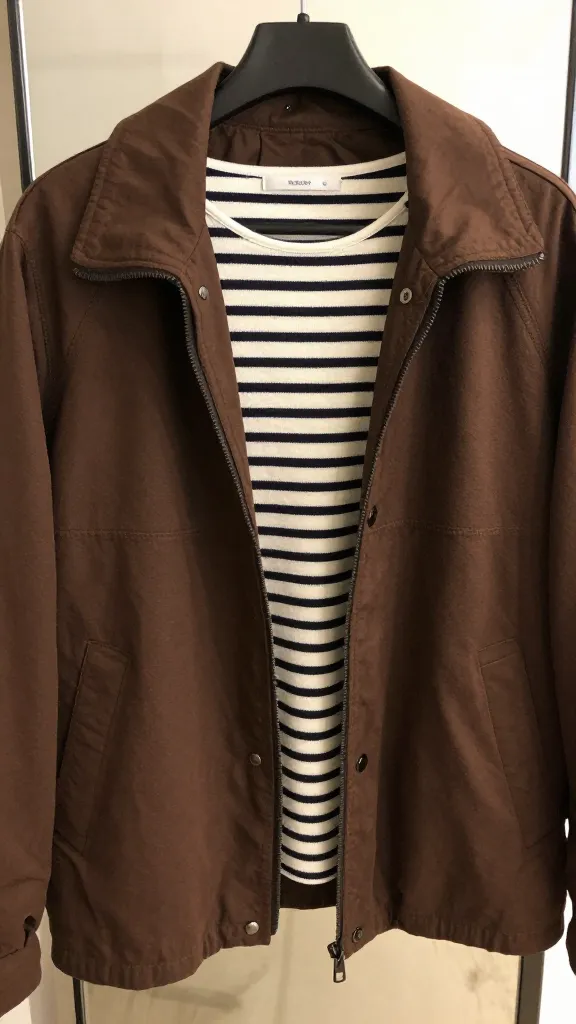 Close-up shot of a medium chocolate brown jacket paired with a striped black-and-cream top, resting on a hanger in front of a mirror, wrists and accessories cropped out.